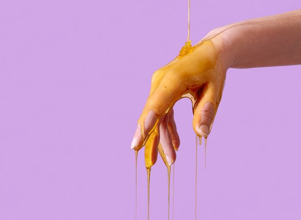 Skin care concept, pouring honey over hand, isolated on a purple background