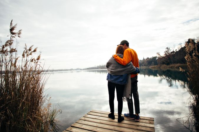 Man and woman embrace on the pier of a lake