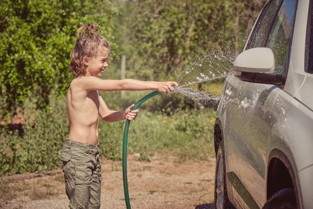 Cheerful boy washing car in countryside