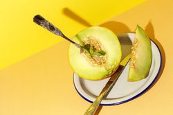Sliced small melon on plate with spoon and fork