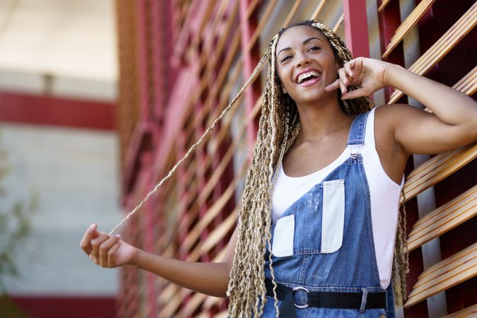 Smiling female in vest and overalls posing near window blinds