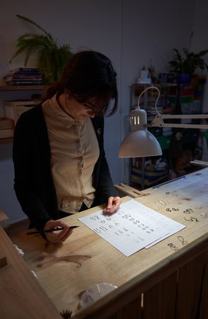 Female goldsmith drawing jewelry pictures at table in dark room