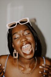 Excited Black woman wearing gold jewelry and framed sunglasses