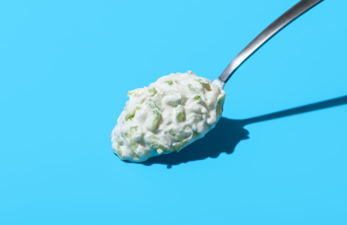 Tzatziki sauce on a spoon, isolated on a blue background