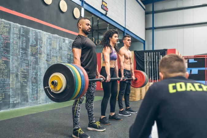 Multiracial team lifting weights in the gym with their coach