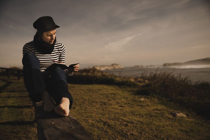 Woman writing in notebook and sitting on bench on shore near water