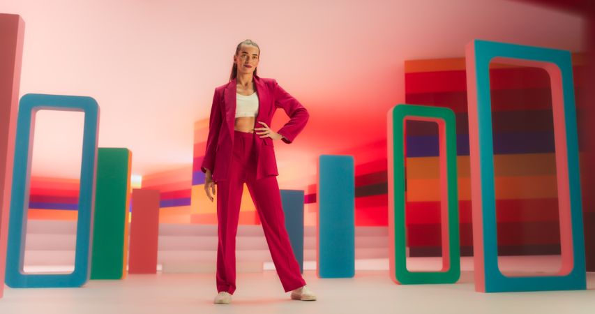 Low Angle Portrait of a Stylish Female Posing Confidently in a Bright Lit Room. Fashionable Young Woman Striking A Pose In Colorful Creative Studio Environment, Working For High Fashion Brand.