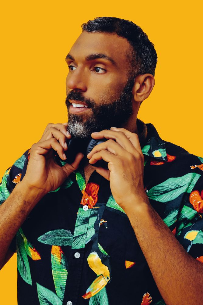 Black male in bold patterned shirt wearing headphones in yellow room, vertical