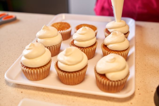 Crop person decorating cupcakes with whipped cream