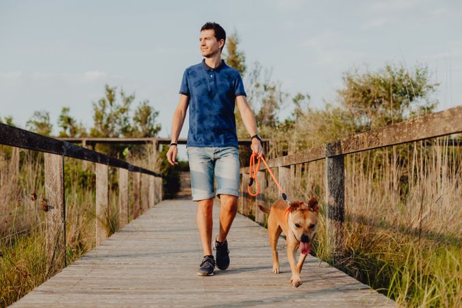 Happy adult man walking with dog along countryside