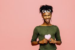Portrait of a smiling young man holding a pink heart, isolated on pink studio background