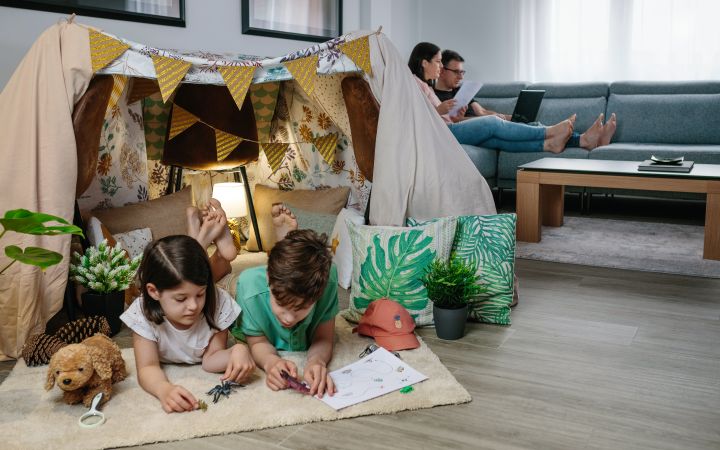 Children playing camping at home while their parents work with laptop