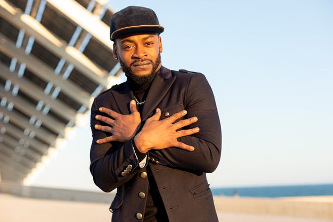 Portrait of stylish Black man standing outdoors in front of modern structure with hands crossed over chest