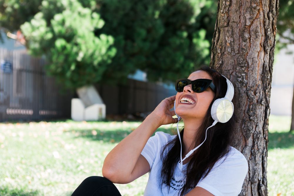 Relaxed trendy woman in headphones resting in park on grass