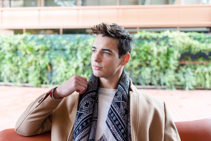 Confident young Young man wearing winter clothes sitting on a leather bench in the street lounging at home on the sofa looking at the camera