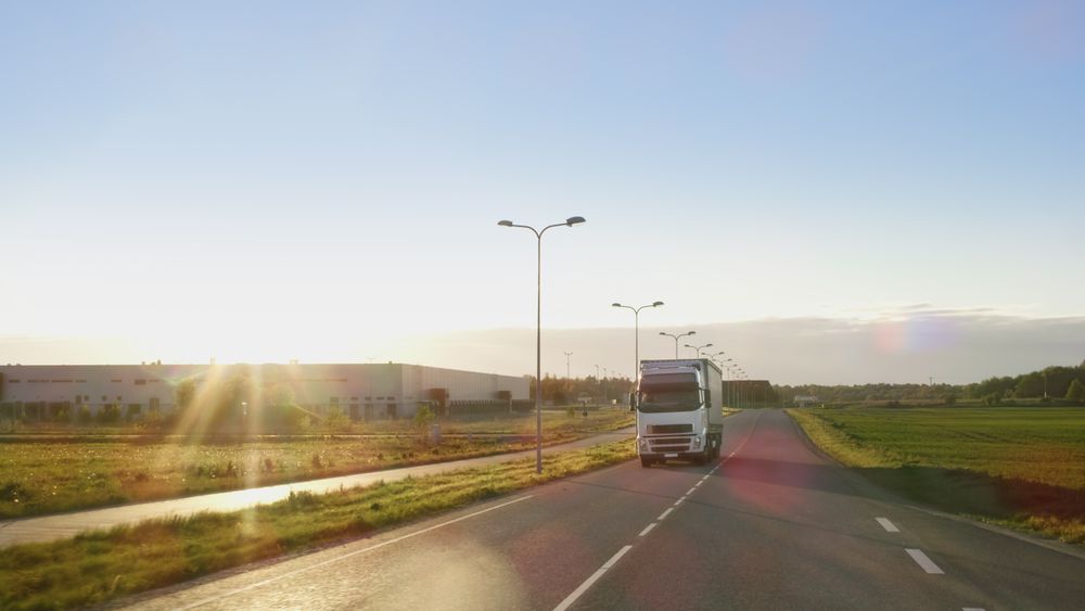 Semi Truck with Cargo Trailer Drives on a Highway with Sunny Scenery in the Background.