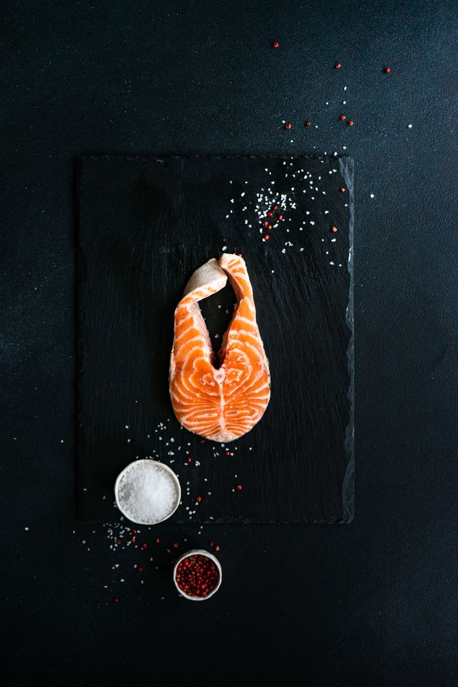 Top view of salmon steak on dark counter with seasoning