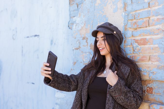 Charming Hispanic lady taking selfie near wall