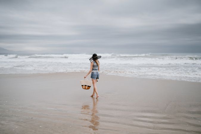 Young female walking barefoot on sandy beach
