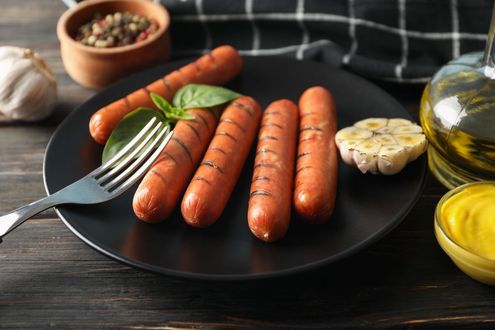 Grilled sausages or hot dogs on a fork on dark ceramic plate with garlic