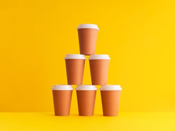 Pyramid of disposable coffee cups on yellow background