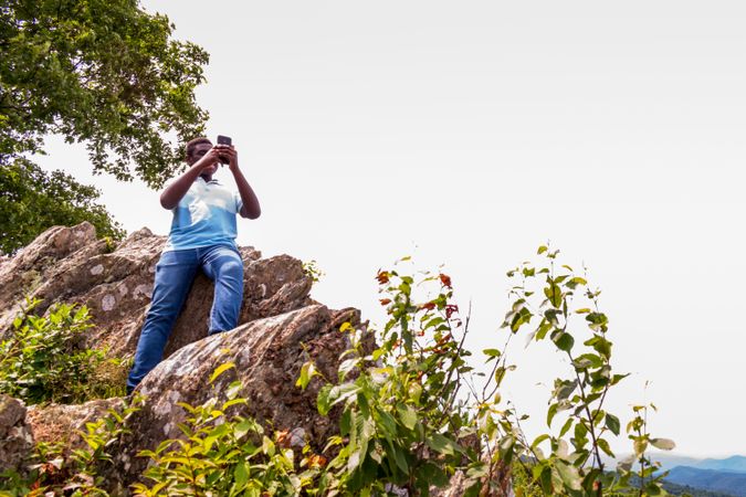 Black person checking his phone sitting on a rock outside