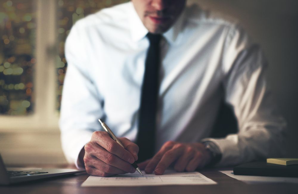 Man in shirt and tie writing on documents late at night