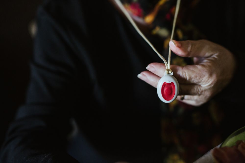 Crop mature woman showing pendant with SOS button