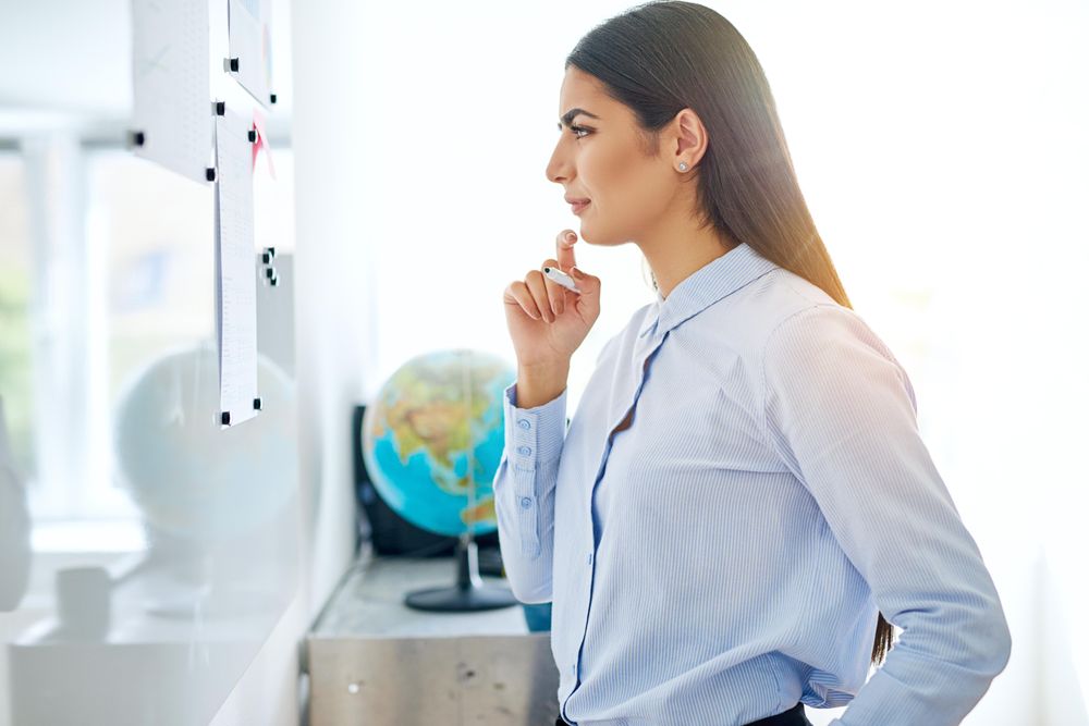 Arab woman pensive as she works through problem on dry erase board