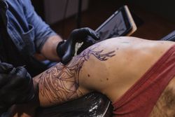 Master doing tattoo on forearm of male customer