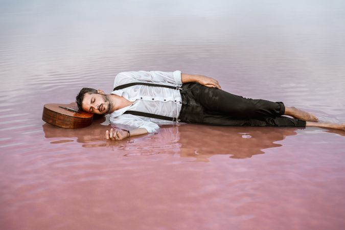 Man resting in water with guitar at seaside