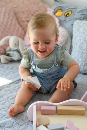 Adorable baby playing with wooden blocks on bed