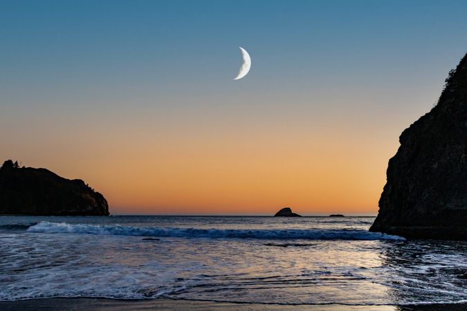 Crescent moon above quiet beach at dusk