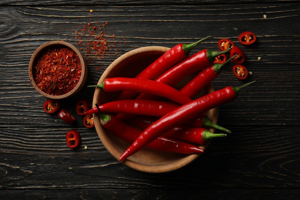 Spices and bowl with chilli pepper on wooden background