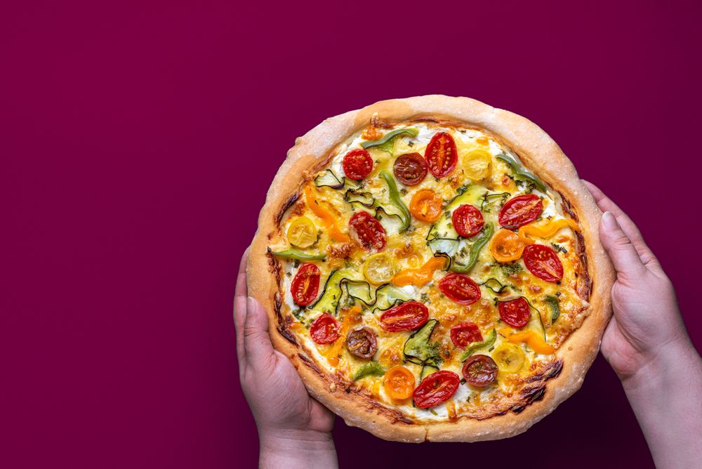 Vegetarian homemade pizza in womans hands against a magenta background