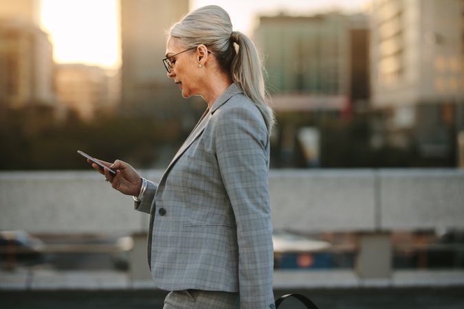 Mature woman reading messages on a smartphone while walking on urban background