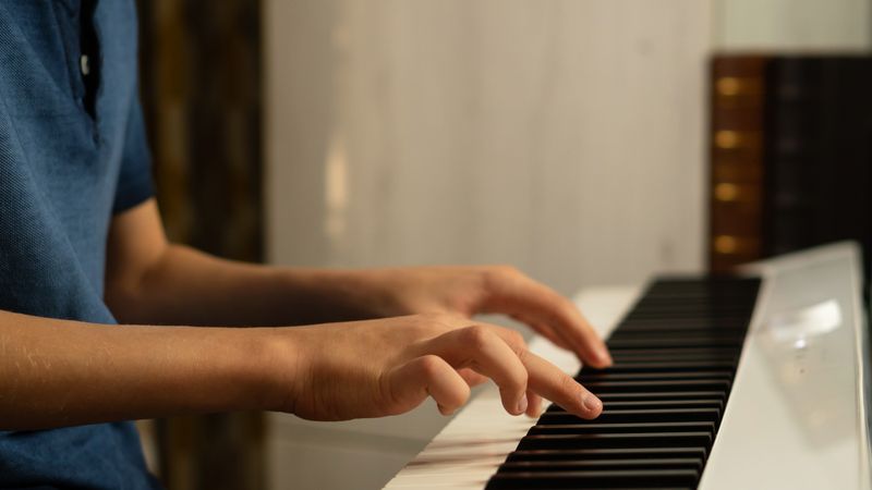 Side view of boy’s hands pressing piano keys on keyboard