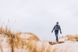 Man walking between sand field with dry grass