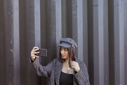 Charming Hispanic lady taking selfie near wall