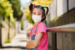 Child in facemask with arms crossed outside