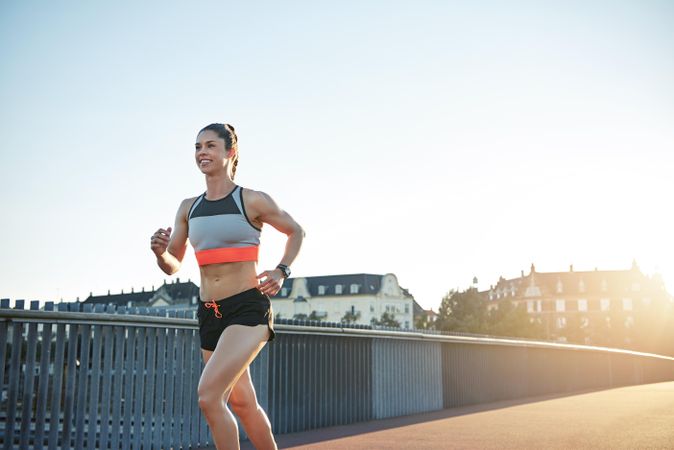 Happy fit woman running cross bridge with sunflare