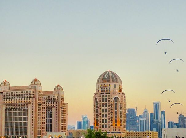 Brown dome top high-rise buildings in Doha, Qatar with parachutes in sky