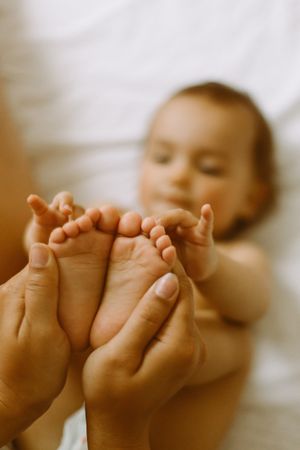 Anonymous mother touching baby feet on bed
