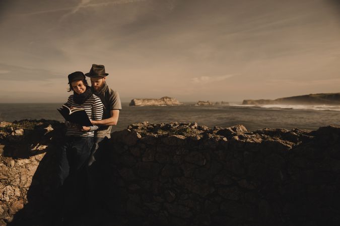 Man near woman with books near stones on shore