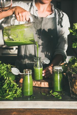 Woman pouring green smoothie into glass jars in kitchen