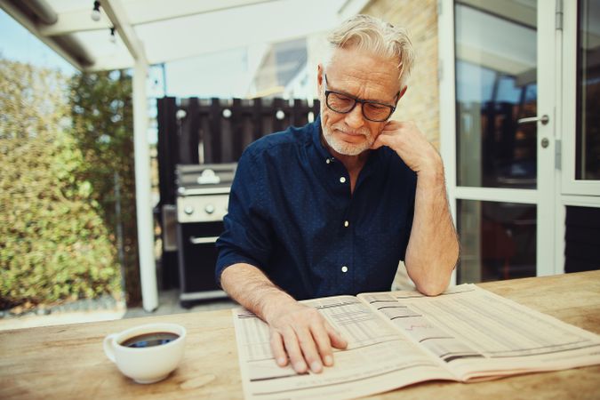 Mature man sitting in his yard reading the paper