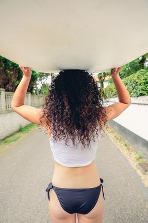 Brunette female holding surfboard over head on street