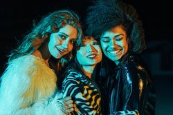 Group of happy female friends lit in green blue light at night