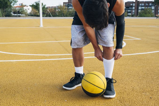 legs of crop Young man and ball playing on basketball court outdoor.
