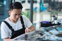 Male applying protective car wrap to front of vehicle